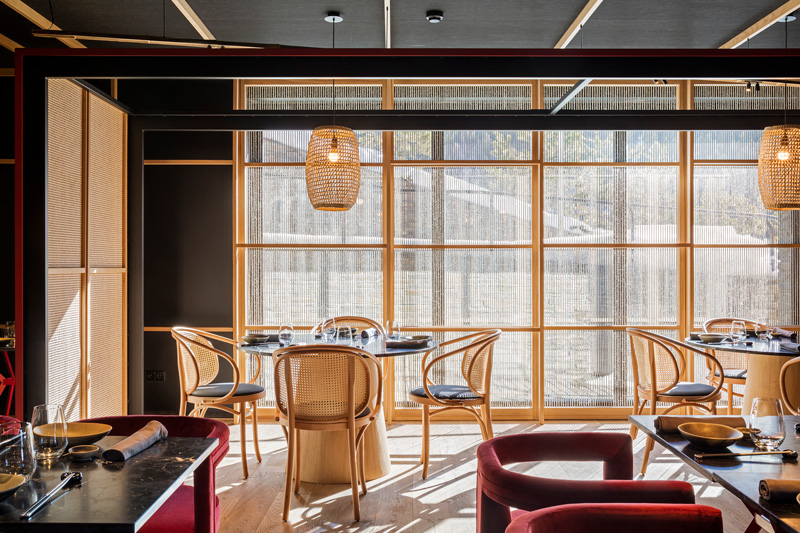 Interior del restaurante Kao Soldeu con la vista de mesas y sillas de madera, mamparas con cuerdas y uso de tapicería de terciopelo rojo en algunas sillas