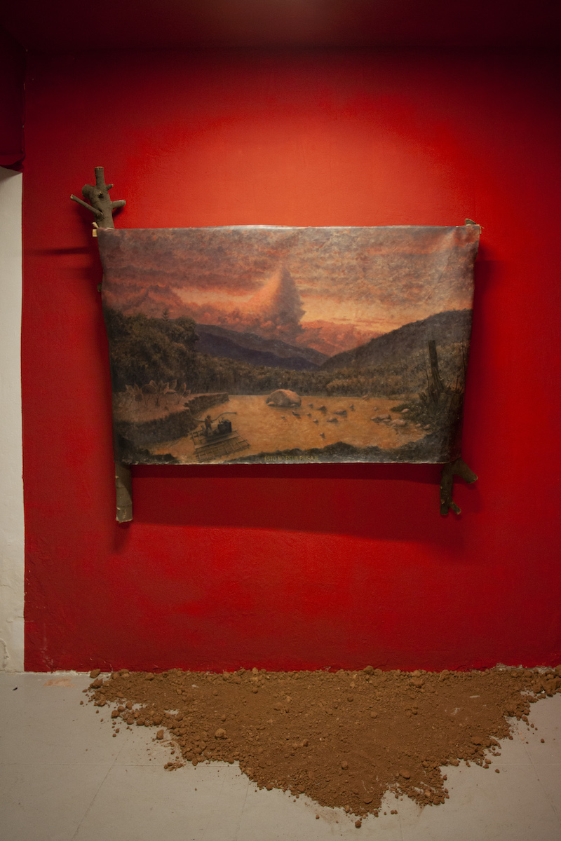 Daniel De la Barra, Instalación de paredes rojas con un cuadro de un paisaje montañoso enmarcado con troncos naturales y tierra en el suelo.