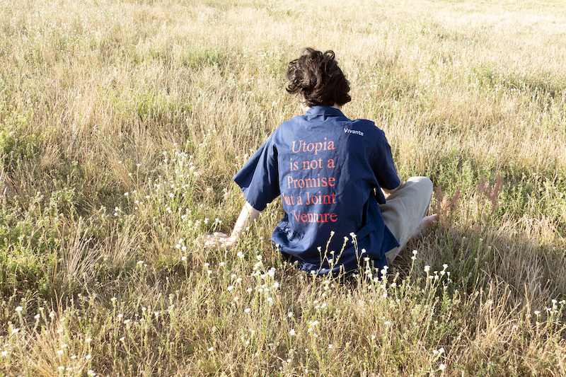 Berlin Art Week 2020 chico con camisa azul de espaldas donde se lee "utopia no es una promesa sino una aventura"