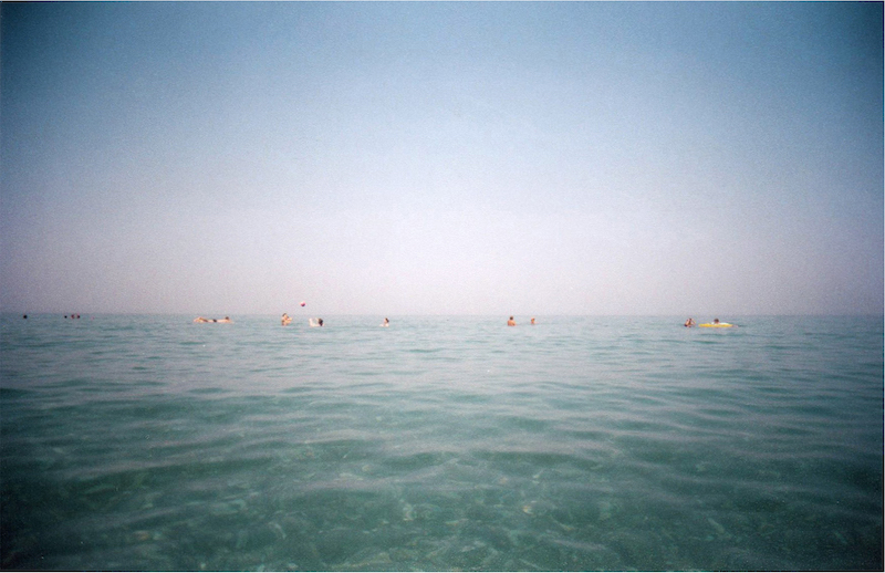 Ineditos 2020_un paisaje de mar azulado con cabezas de bañistas lejos