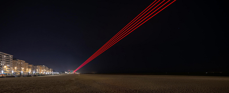 SpY_artista urbano. 5 haces de laser rojo en una playa por la noche 