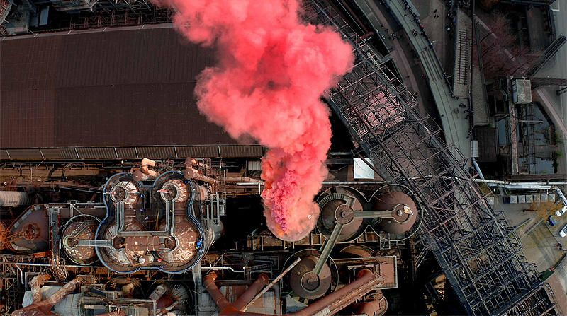 SpY_artista urbano. humo rojo sale de una chimenea de una fábrica, vista cenital