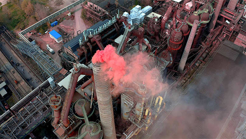 SpY_artista urbano. humo rojo sale de una chimenea de una fábrica, vista aerea