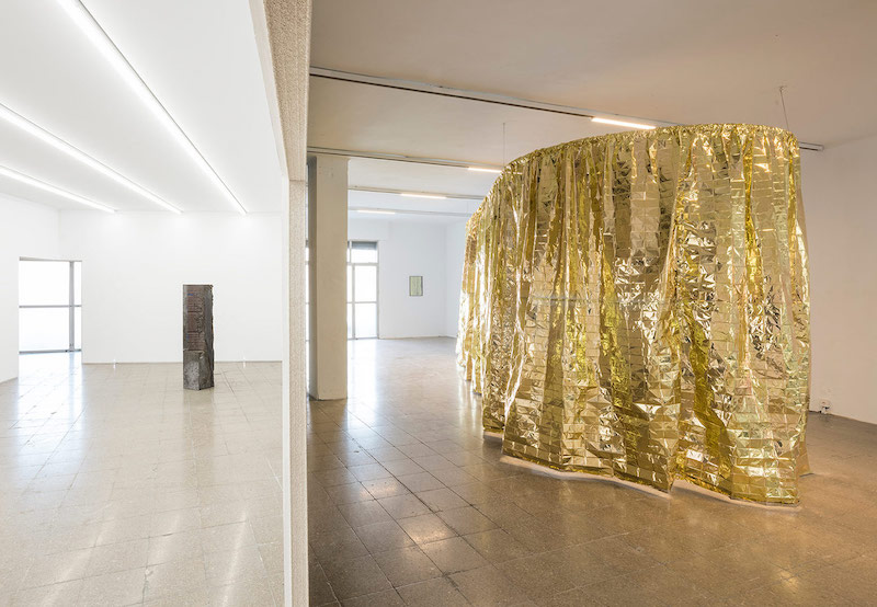 Aliento, Celine Condorelli, a la derecha una cortina dorada y en la otra habitación una escultura de forma totémica de hormigón