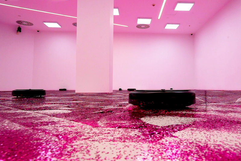 Canal Connect, una instalación artística con un robot de limpieza redondo y el suelo de purpurina rosa