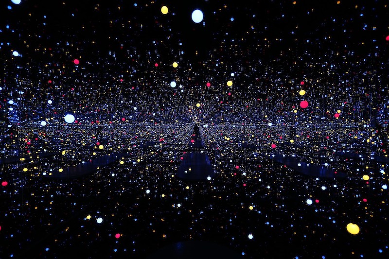 Yayoi Kusama, instalacion llena de luces a modo de puntos de color. En la habitación hay columnas, esta rodeada de espejos y cuadrados en el suelo