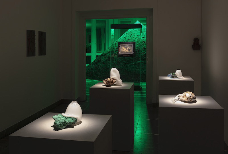 Schinkel Pavillon, una habitación con podiums y esculturas de video y roca y al fondo una habitacion dende se ve una montaña iluminada de verde