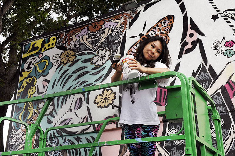 Lady Aiko - la artista posando en un andamio delante de uno de sus murales
