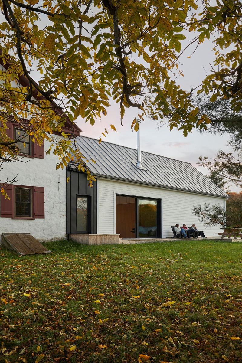 maison denison adhoc architectes: imagen del anexo de una casa con varias personas sentadas en la puerta