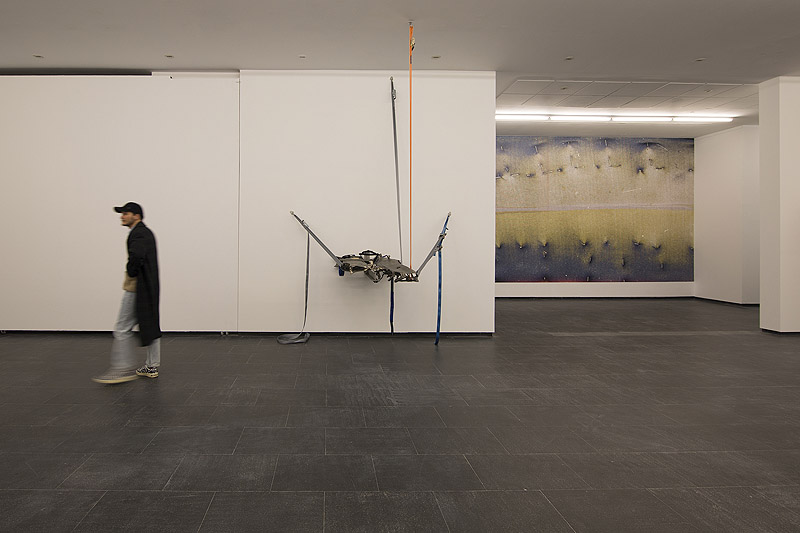 Exposiciones en el CA2M - vista de la exposición, visitantes contemplan una escultura hecha con desechos industriales sujeta en una pared