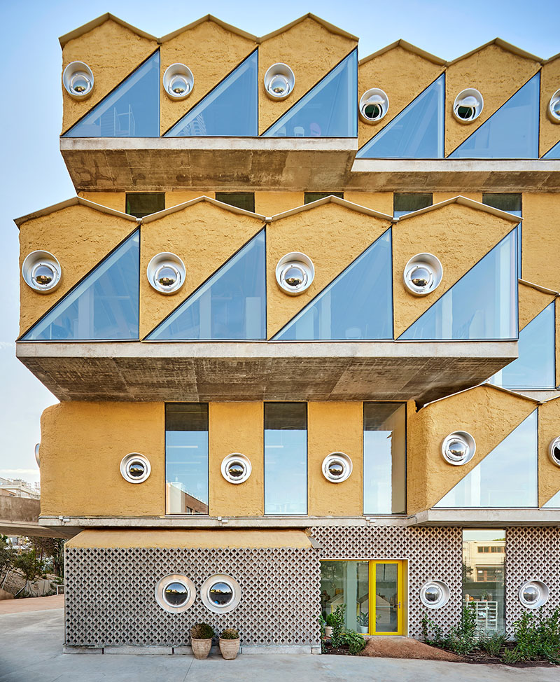 Reggio School de André Jaque: vista del edificio de colores mostaza y ventanas triangulares y redondas