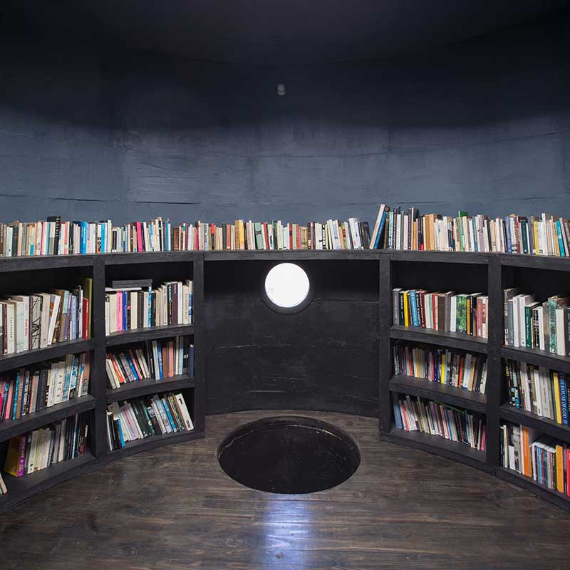 Casa Luna de Pezo Von Ellrichshaushen. Biblioteca con estantería de madera repleta de libros. Fachada curva y ventana circular al exterior.