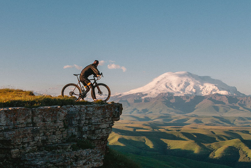 Paradores y ciclismo en Otoño: un ciclista en el pico de una montaña observando una montaña nevada