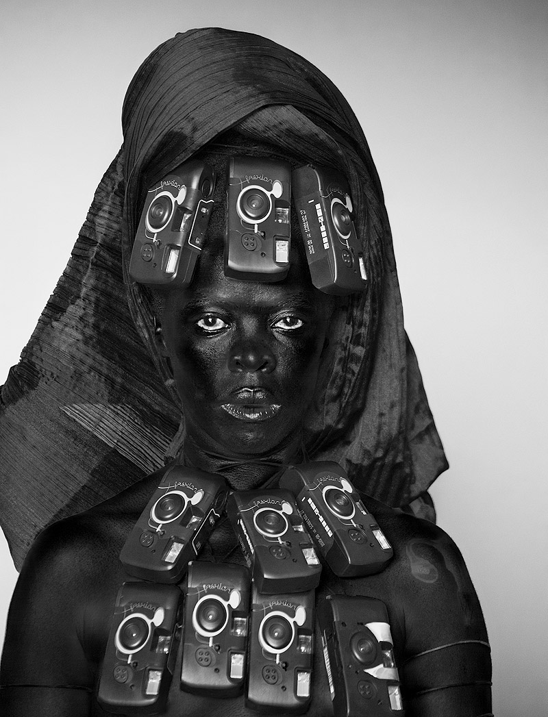 Zanele Muholi. Eye Me. Imagen de una mujer negra con un turbante y con la cara y el cuello cubiertos de cámaras.