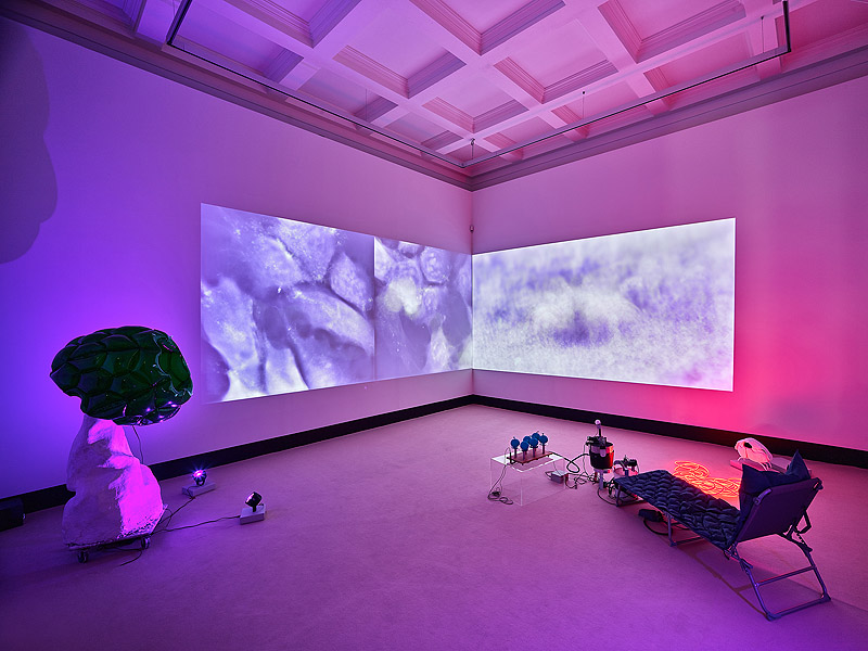 "Loving the Alien". Imagen de la exposición con una pantalla gigante e iluminación morada.