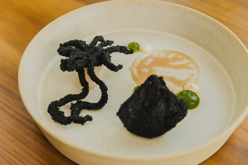 Abya: Chipirón Black andaluza, rebozado en tinta liofilizada con jugo de chipirón al wok y alioli de alga codium, perteneciente al menú de 65 euros