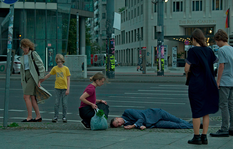 musica - imagen de la película, se ven a personas por la calle una está tirada en el suelo