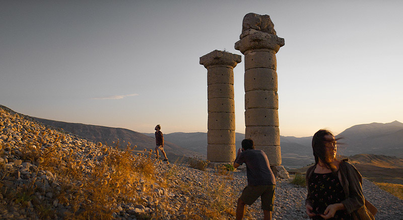 Sobre la hierba seca - fotograma de la película se ve a 3 personas paseando por unas ruinas romanas