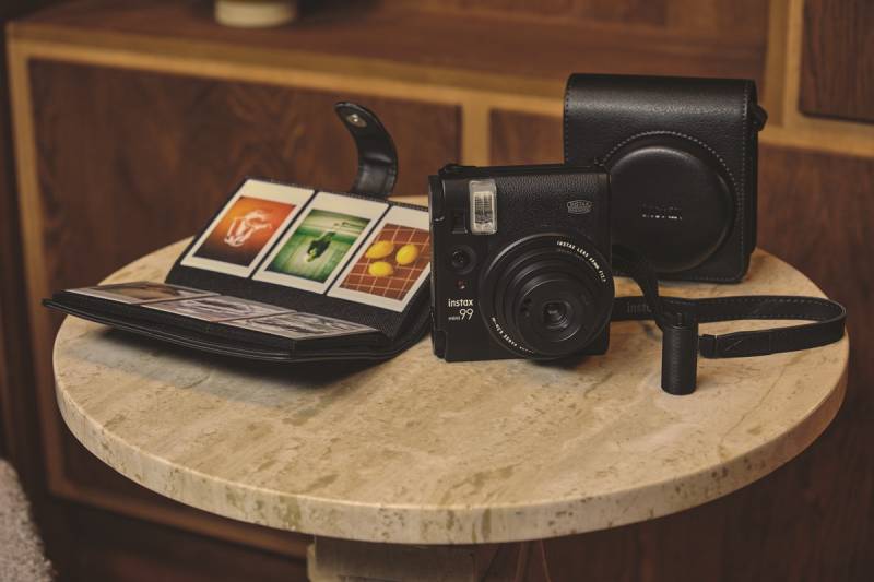 Instax Mini 99: la cámara Instax Mini 99 sobre una mesa con la funda y un álbum.