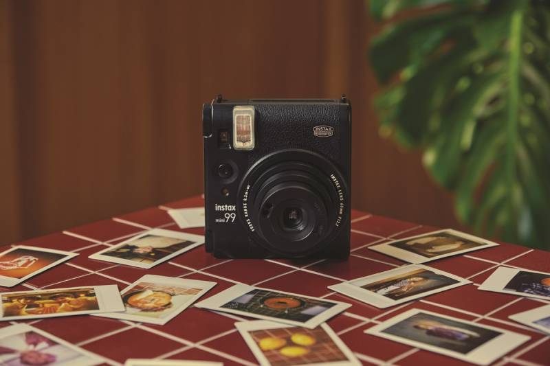Instax Mini 99: la cámara Instax Mini 99 sobre una mesa con unas cuantas fotos por encima.