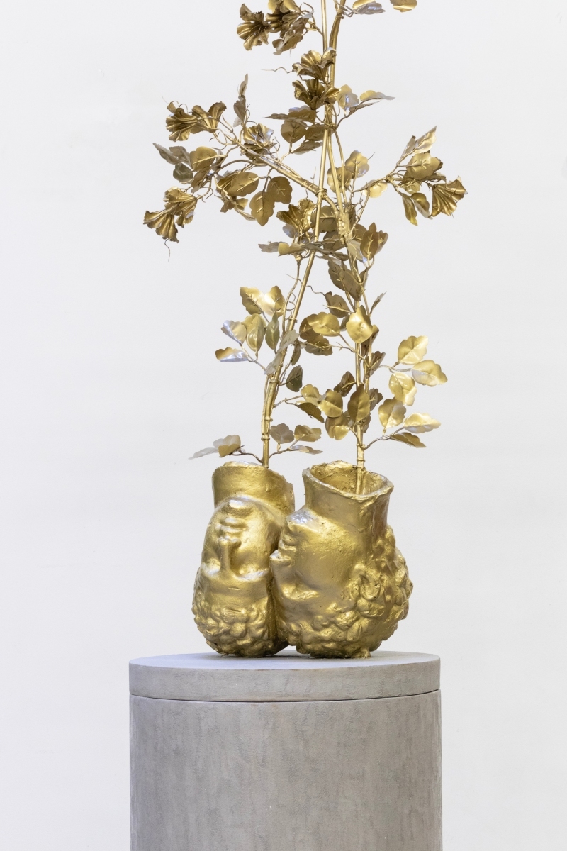Leo Fourdrinier. Imagen de escultura de cabezas boca abajo con plantas doradas.
