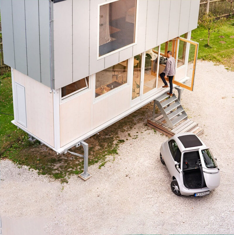 Microlino automóvil: Un Microlino blanco aparcado frente a una casa en la que entra un hombre