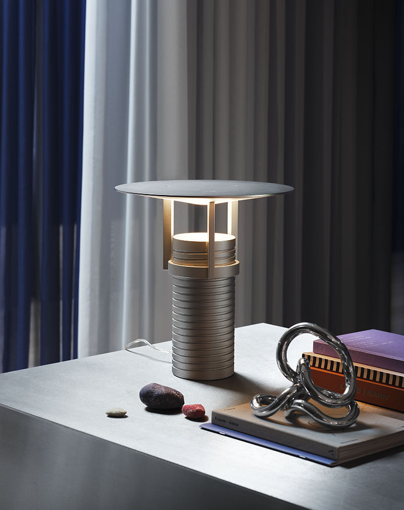 Muuto Set Lamp: la lámpara con forma de tornillo fabricada en aluminio encima de una mesa con unos libros y piedras