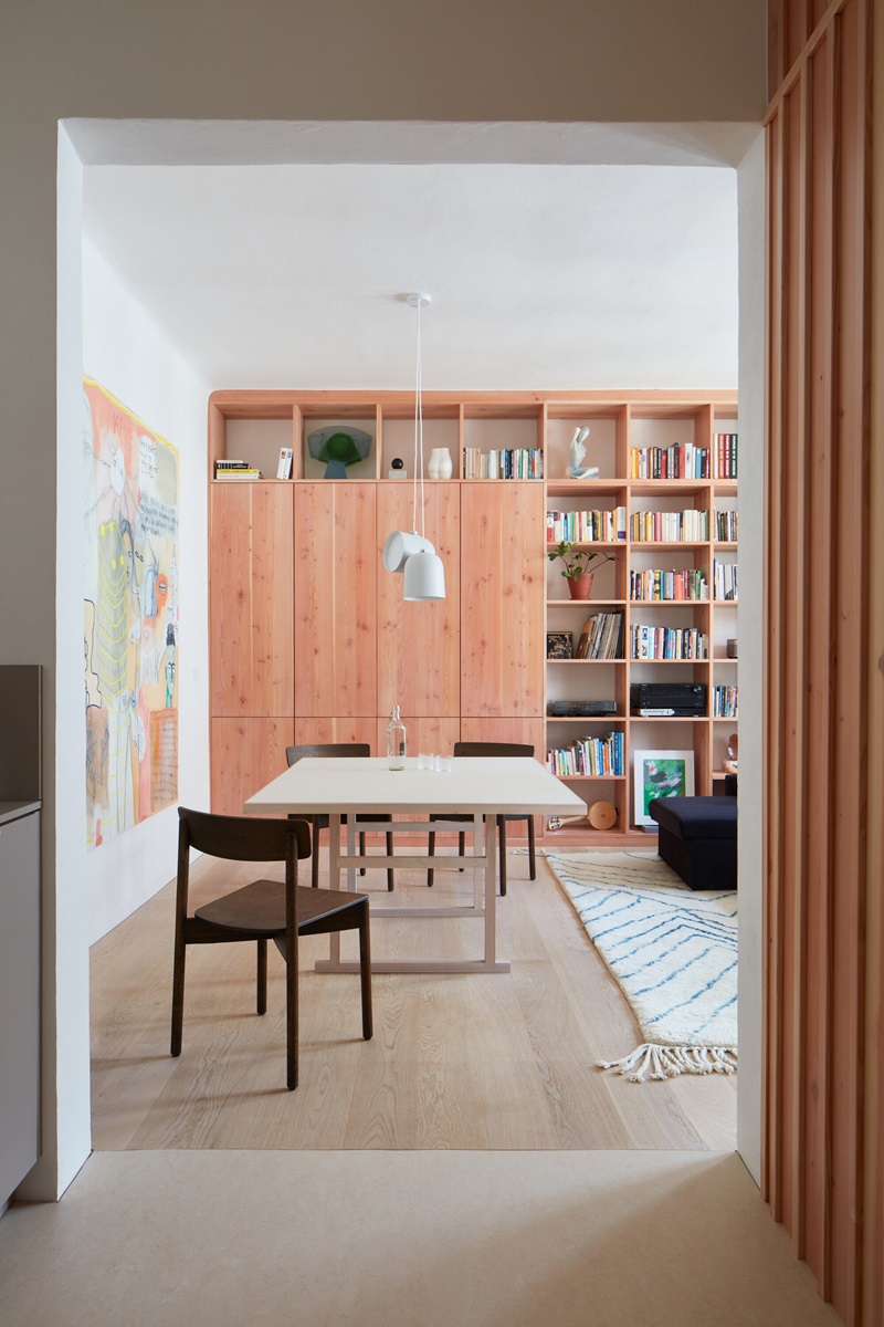 Plus-One-Architects- Vršovice-Apartment: estantería de madera con libros en el salón y mesa de comedor