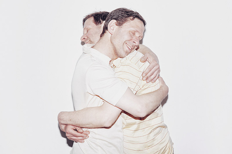 Revela't. Imagen de dos hombres vestidos de blanco abrazándose.