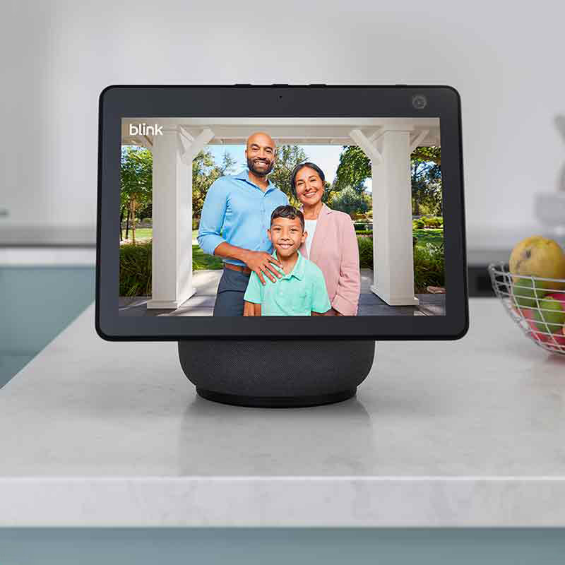 Blink Video Doorbell: una tablet sobre una encimera muestra una familia, compuesta por un padre, una madre y un hijo, esperando a que le abran la puerta de una casa con jardín tras haber llamado al timbre de Blink Video Doorbell.