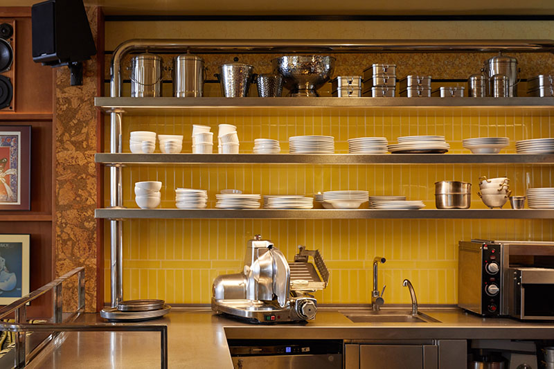 Casa Fiero muestra una estantería metálica con vajilla blanca y fondo de azulejo amarillo