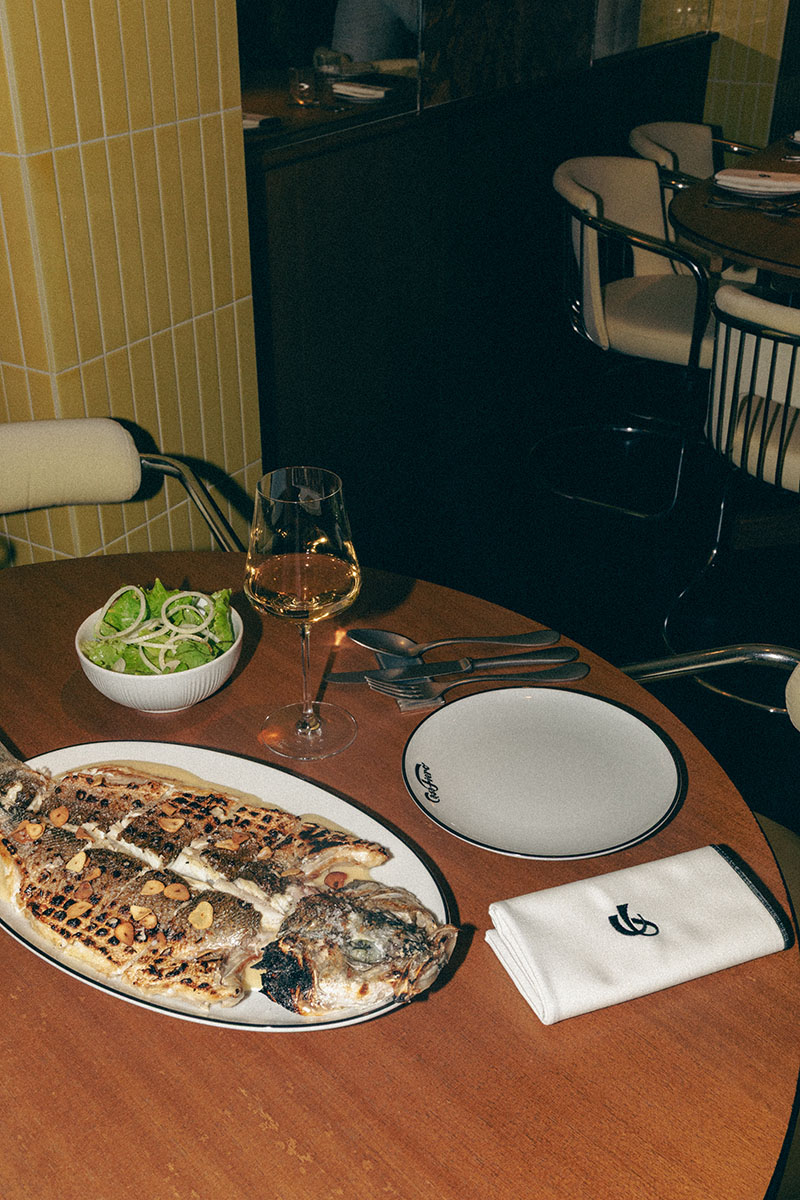 Casa Fiero presenta una mesa redonda con pescado a la brasa, ensalada y copa de vino