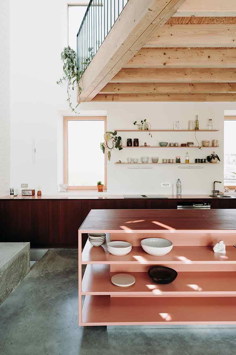 Vista de la cocina de Casa Lyco, diseñada por Oyo Architects, con isla central en color salmón y mobiliario oscuro a medida