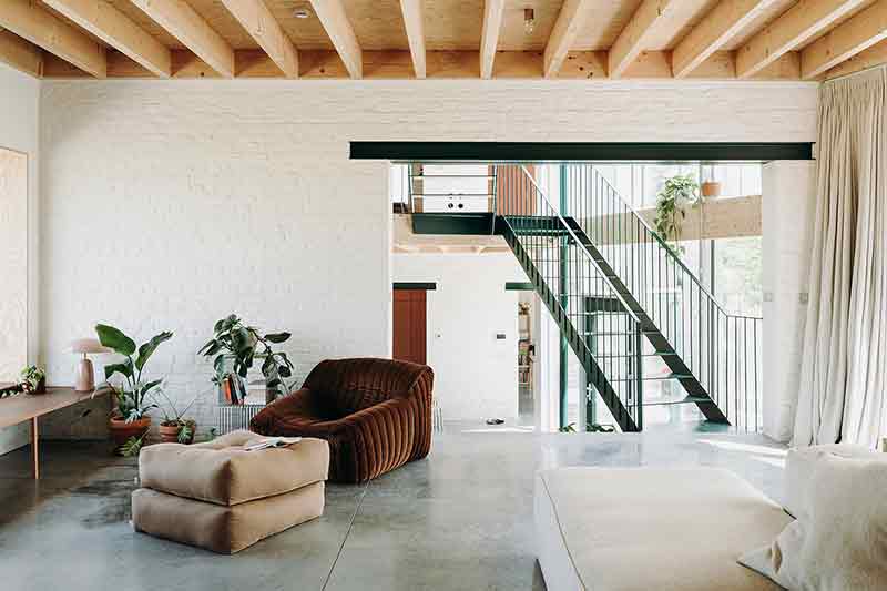 Zona de estar en Casa Lyco, proyecto de Oyo Architects, con pavimento continuo, techos de madera y mobiliario bajo