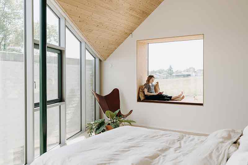 Dormitorio de Casa Lyco, obra de Oyo Architects, con techos inclinados, carpinterías a medida y ventana tipo nicho