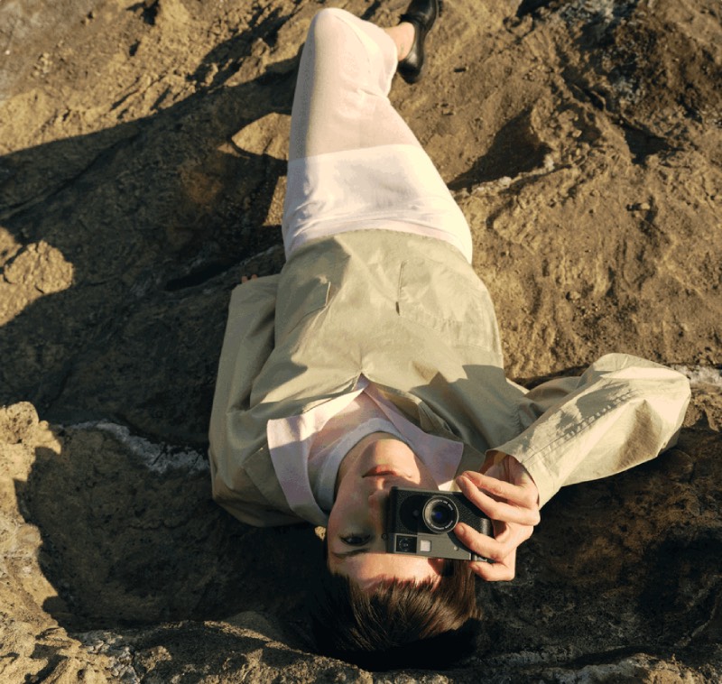 Fujifilm X half: plano cenital de una mujer tumbada sobre un terreno rocoso realizando una fotografía con la cámara digital compacta Fujifilm X half.