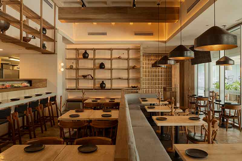 Interior de SC | Nido Cancún diseñado por Neutro Estudio con barra, mesas y estantería de madera