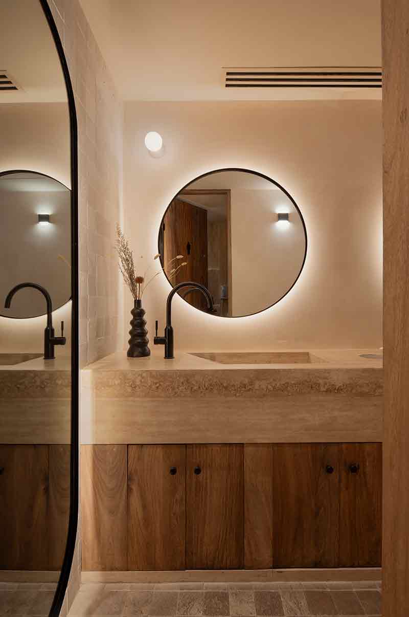 Baño de SC | Nido Cancún diseñado por Neutro Estudio con lavabo de travertino y espejo circular retroiluminado