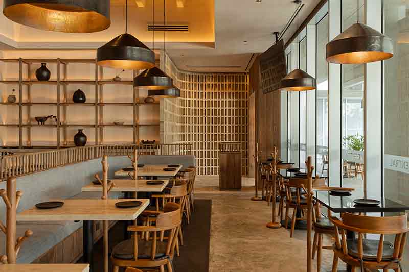 Zona de mesas de SC | Nido Cancún proyectada por Neutro Estudio junto a ventanales y luminarias de cobre