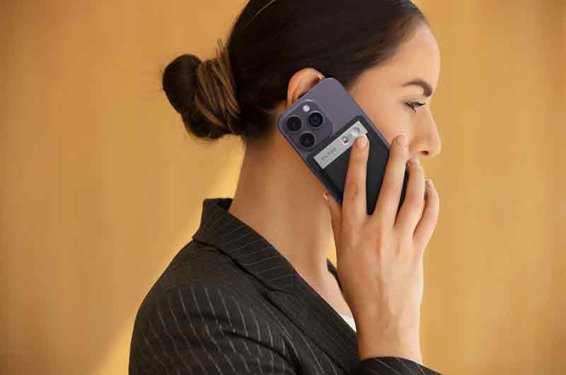 Plaud Note: primer plano de una mujer de piel clara con un moño bajo sobre un fondo mostaza que graba una conversación que mantiene por teléfono con Plaud Note.