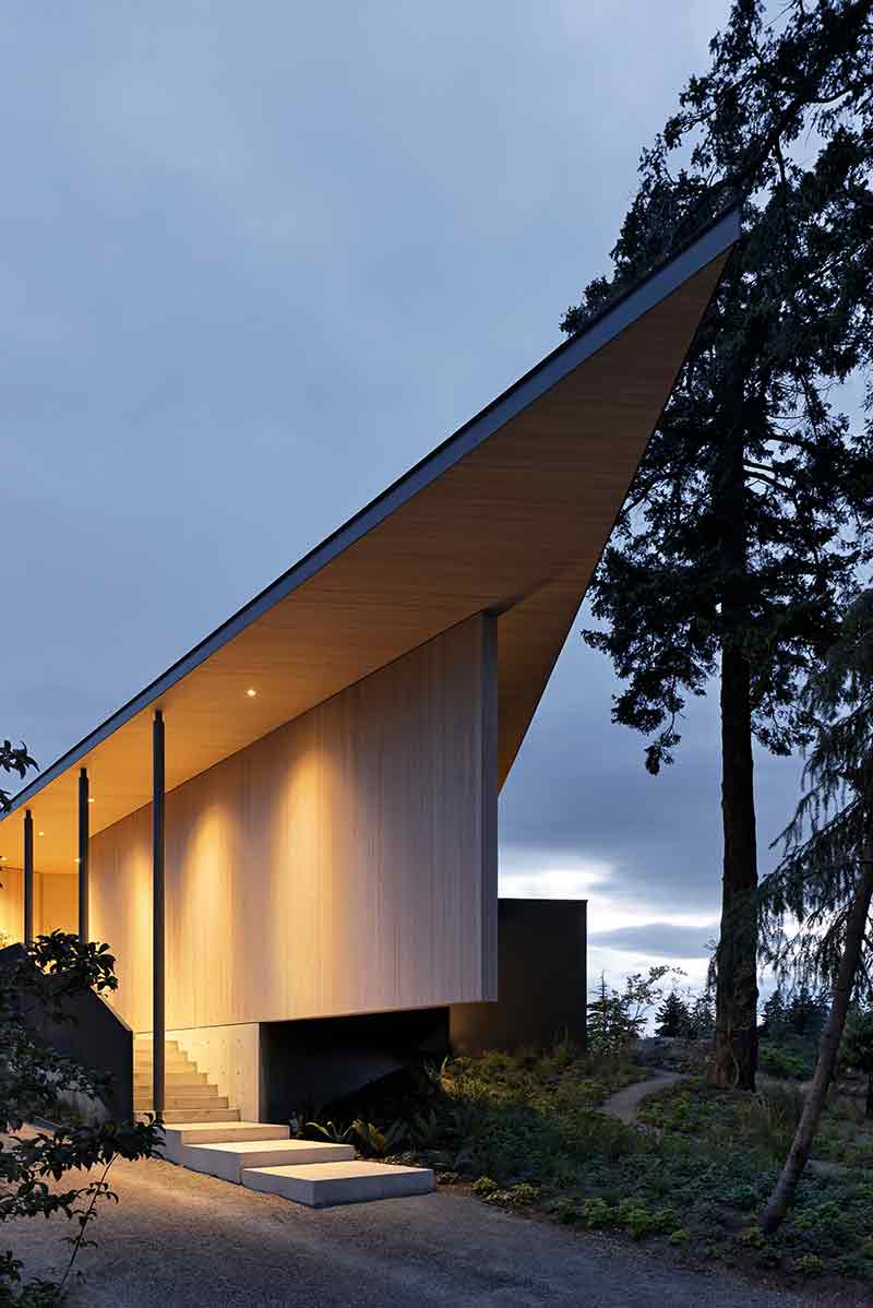 Shoreline House de Splyce Design muestra un acceso elevado con cubierta afilada y muros de madera clara.