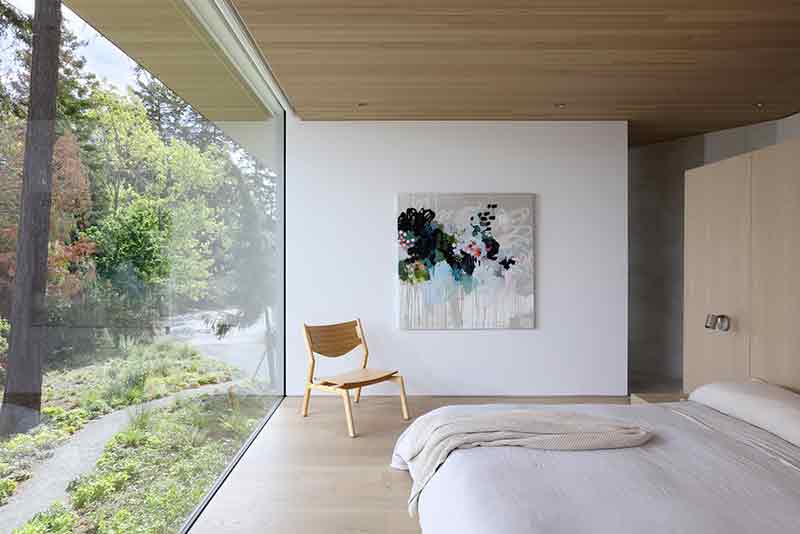 Shoreline House de Splyce Design integra el dormitorio principal con el entorno natural a través de un ventanal completo.