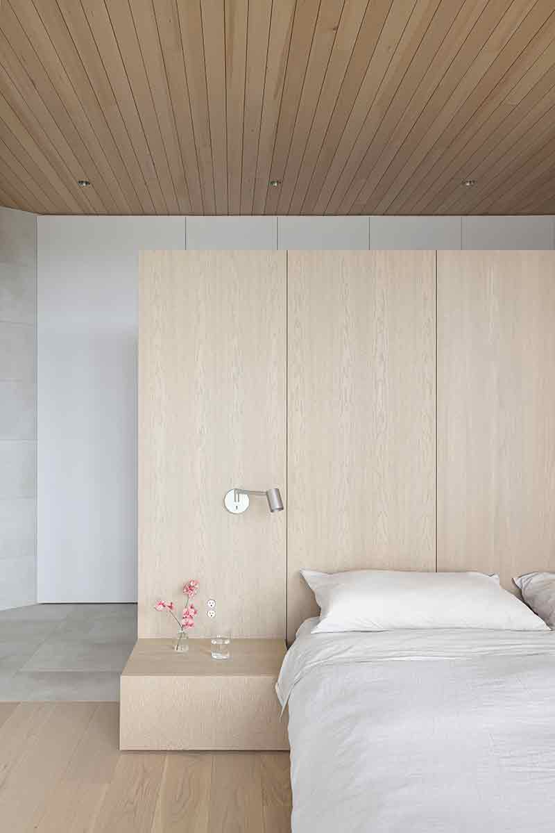 Shoreline House de Splyce Design configura el dormitorio con mobiliario minimalista y acabados en madera clara.