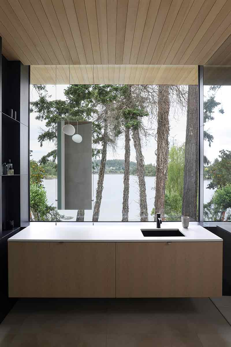 Shoreline House de Splyce Design incorpora un fregadero enmarcado por un ventanal con vista directa al paisaje costero.