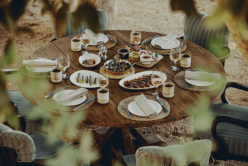 Soho Farmhouse Ibiza: mesa redonda con varios platos de comida y copas de vino en comedor al aire libre