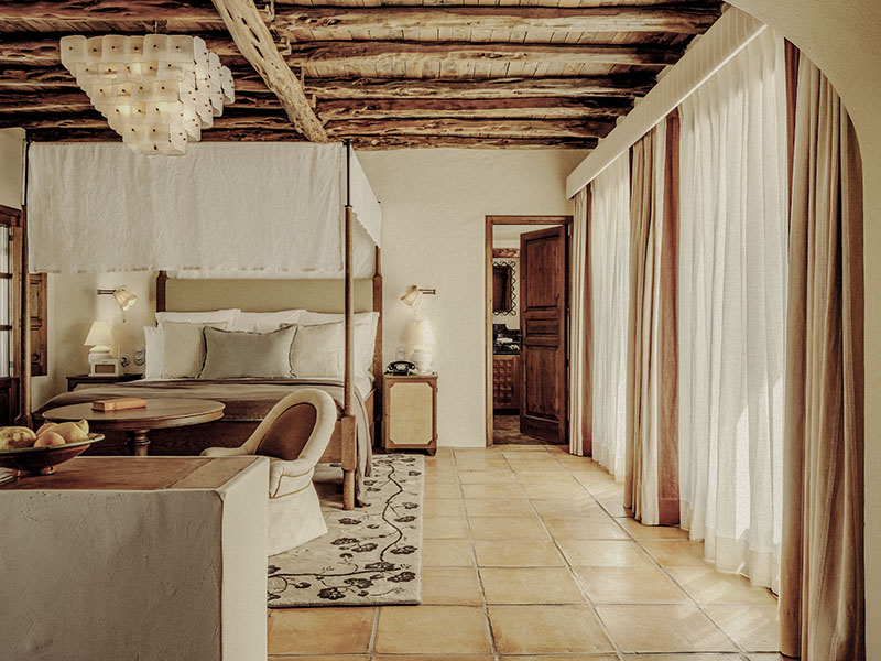 Soho Farmhouse Ibiza: dormitorio con cama con dosel, vigas de madera y suelo de terracota