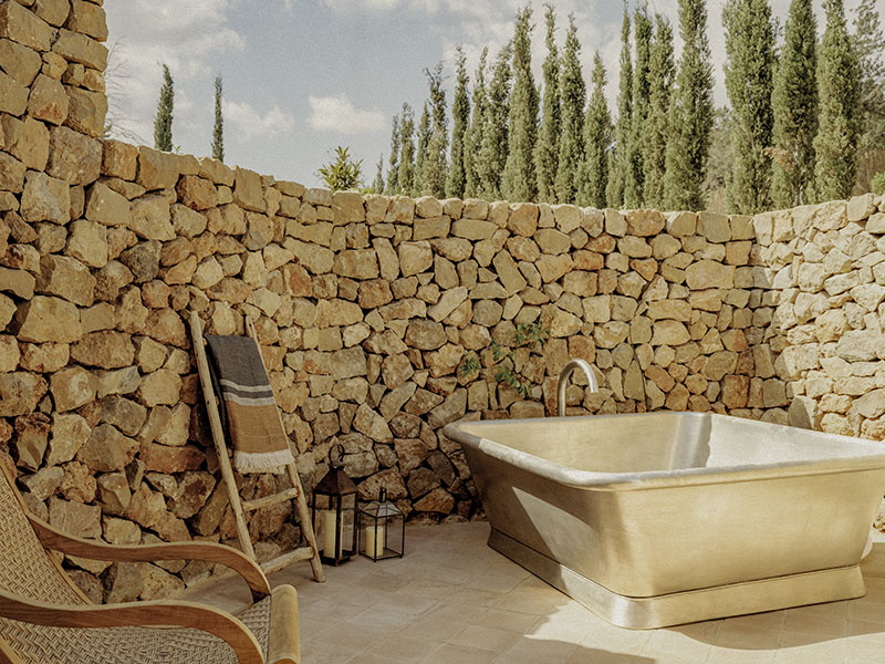 Soho Farmhouse Ibiza: bañera exterior rodeada de muro de piedra y mobiliario de madera