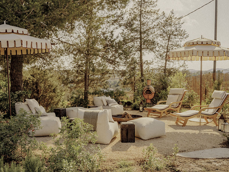 Soho Farmhouse Ibiza: zona exterior con sofás, sillones, tumbonas y sombrillas entre vegetación y árboles