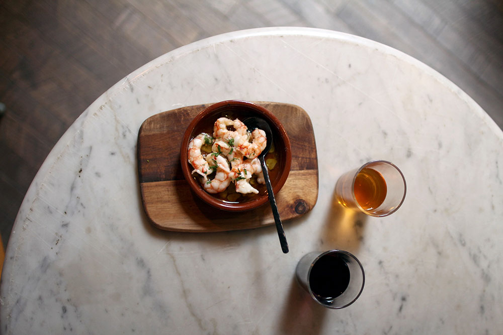 Gambas al ajillo con dos copas de vino en mesa de mármol en Tapas Lobito Barcelona