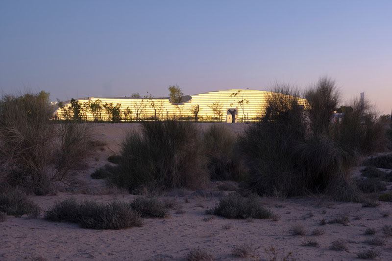 Vista nocturna iluminada del Centro de Experiencia Ghaf Woods diseñado por Aoe estudio arquitectura china desde el desierto